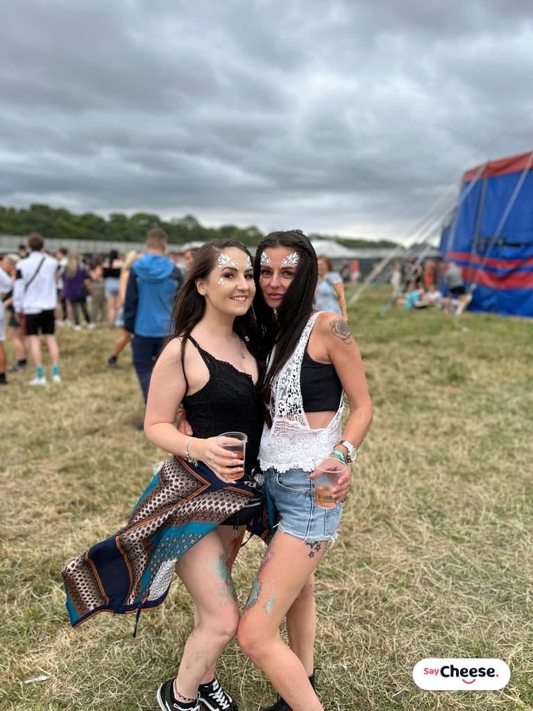 Two friends with glitter face paint arm in arm at a festival