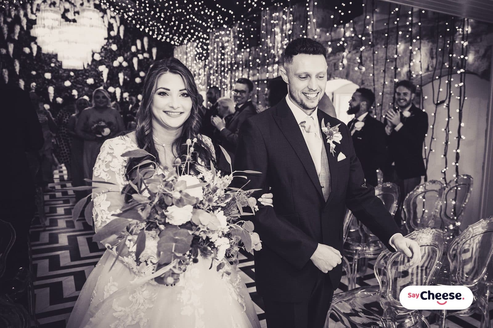 A newly married couple walking back down the aisle under fairy lights